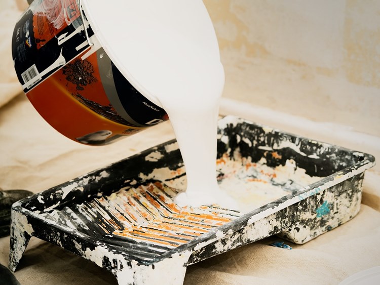 White paint pouring from paint can into drip tray