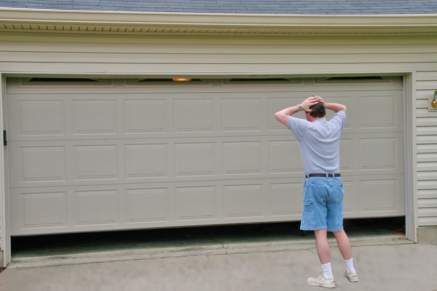 Exasperated man holding head in hands in confusion about stuck garage door