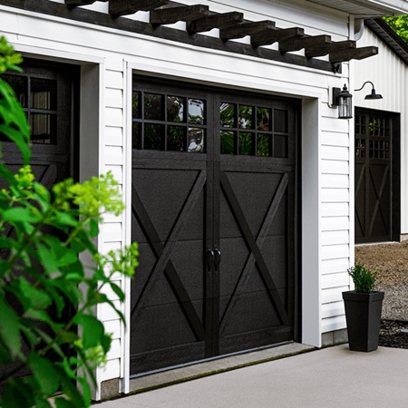 Black carriage house garage door with black metal hardware on white paneled garage